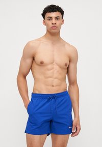 Shorts de bain bleus en tissu léger, avec une taille à cordon de serrage et un accent logo sur la jambe gauche.