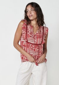 Blusa senza maniche a righe rosse e bianche con rifiniture arricciate e dettaglio con laccio frontale. Realizzata in tessuto leggero e traspirante.