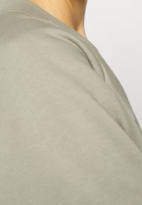 Koszulka z bawełny w kolorze oliwkowym, z okrągłym dekoltem i luźnym krojem. Miękka w dotyku z gładkim wykończeniem, uwydatniająca detal szwu na ramieniu.