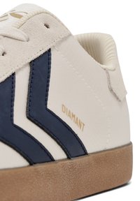 Sneaker bej cu accente albastre în zigzag, dotat cu un material texturat, branding auriu "DIAMANT" și o talpă din cauciuc maro.