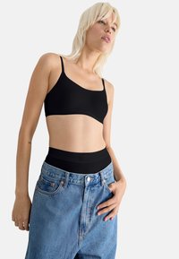 Black bralette made of smooth fabric, featuring slim adjustable straps. Paired with high-waisted light blue denim shorts with a casual fit.