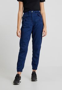 Mörkblå denim joggerbyxor med resårmidja och mudd, med sidofickor och avslappnad passform. Styla med en svart skjorta och sneakers.