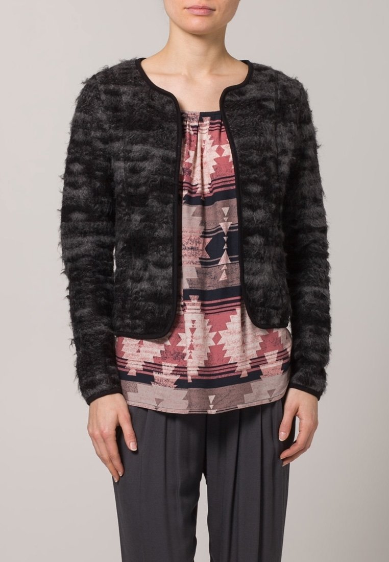 Cárdigan negro texturizado con cuello redondo, ribete en contraste, que se lleva sobre una blusa estampada con diseños geométricos en rosa y azul marino.