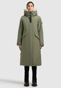 Olivengrøn lang frakke med en hætte foret med kunstpels, lynlås foran, to sidelommer og justerbare manchetter. Glat stof, minimal hardware.