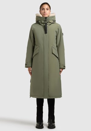 Cappotto lungo verde oliva con cappuccio foderato in pelliccia sintetica, chiusura frontale con zip, due tasche laterali e polsini regolabili. Tessuto liscio, hardware minimale.