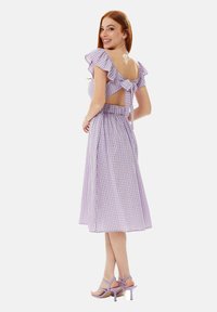 Purple gingham dress with ruffled sleeves, open back, and tied detail. Knee-length, elastic waistband, paired with lavender heeled sandals.