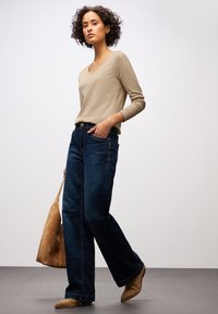 Beige gerippter Langarmtop, dunkelblaue weite Jeans, handtasche aus tanfarbenem Wildleder und hellbraune Stiefeletten, mit einem lässigen Schnitt und natürlichen Texturen.