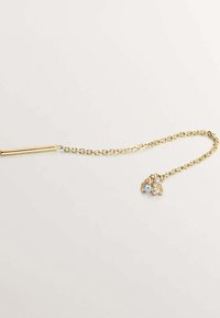 Collar de cadena de oro con un barra cilíndrica y un colgante con tres piedras transparentes, destacando un diseño suave y texturizado.