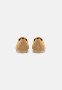 Pantofi din suede bej, cu o textură netedă, tocuri rotunjite și un design minimal. Partea din spate are un detaliu mic în formă de buclă.