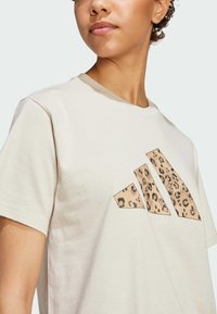 Beige katoenen t-shirt met een grote luipaardprint van drie hoekige vormen op de voorkant; ronde halslijn en korte mouwen.