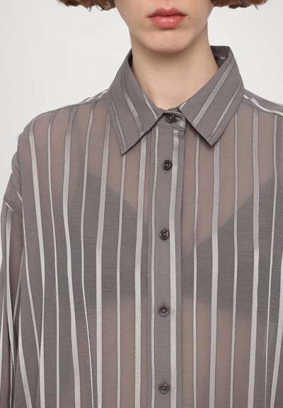 Camicia grigia trasparente con bottoni, a righe verticali di un grigio più chiaro. Presenta un colletto e bottoni scuri. Tessuto morbido e leggero.