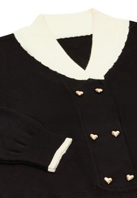 Cardigan tricotat negru cu un guler alb cu dungi, având butoane aurii în formă de inimă și manșete cu dungi. Textură moale pe toată suprafața.