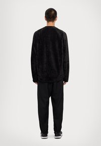 Μαύρη φλις μπλούζα με υφή, στρογγυλή λαιμόκοψη και μακριά μανίκια, σε συνδυασμό με χαλαρές μαύρες φόρμες και αθλητικά παπούτσια.