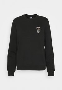 Svart sweatshirt i bomullsblandning, med ribbad rund halsringning och muddar, samt en liten broderad karaktärsdetalj på bröstet.