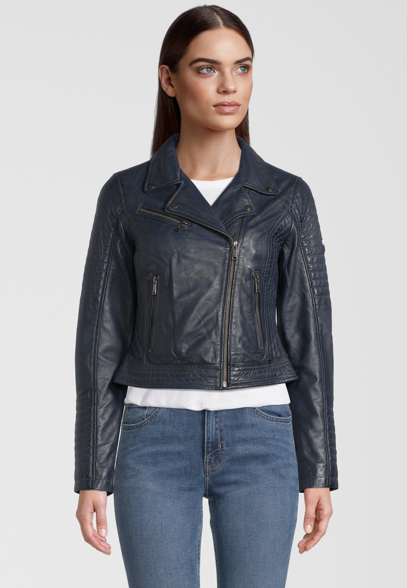 Veste de moto en cuir bleu marine avec un design court, des fermetures éclair argentées, des détails matelassés aux épaules et un large col. Portée par-dessus un haut blanc.