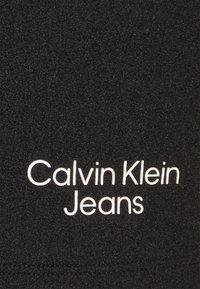 Tessuto nero con la scritta "Calvin Klein Jeans" in grassetto bianco, dalla texture liscia e elasticizzata e un design semplice.