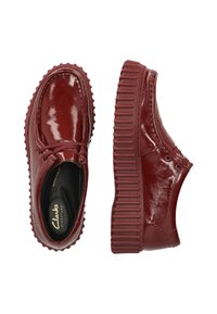 Scarpe in pelle verniciata rossa con punta arrotondata e suola spessa e scanalata. Presentano un design con lacci e una finitura liscia e lucida.