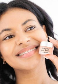 Reparatur von Lippenbalsam in einem kleinen, runden, matten Glasbehälter mit einem silbernen Deckel; das Produktetikett trägt die Aufschrift "berry smooth" in weißer Schrift.