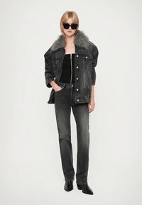 Melna džinsa jaka ar pelēku mākslīgā kažokāda apkakli, kopā ar tumšām džinsām un melniem zābakiem ar papēdi. Modelis valkā melnu augšu un saulesbrilles.