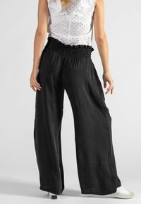 Schwarze, weit geschnittene Hosen aus leichtem Stoff mit einem gerafften Bund. Sie verfügen über einen lässigen Schnitt und werden mit weißen Sneakers kombiniert.