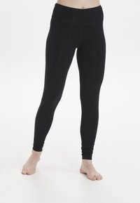 Leggings noirs en tissu extensible avec une taille haute, présentant une texture lisse et une coupe ajustée. Pas de motifs visibles ni de quincaillerie.