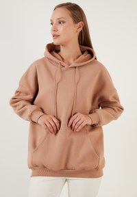Jasnobrązowy hoodie wykonany z miękkiego materiału, z przednią kieszenią, sznurkami i ściągaczami. Luźny krój z gładką fakturą.