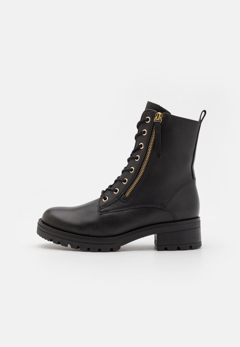 Zwarte leren enkelboot met gouden hardware, veters aan de voorkant, zijrits, en een dikke, gestructureerde zool. Heeft een blokhak en een lus aan de achterkant.