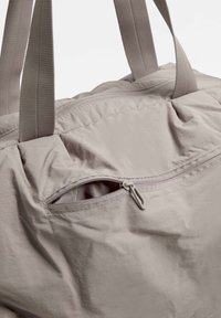 Vaaleanharmaa kangaskassi, jossa on kahdet kahvat, vetoketjullinen tasku edessä ja sileä, hieman rypistynyt pinta.