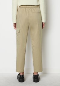 Lichte beige broek met een elastische tailleband, zijcargo zak, rechte pijpdesign en een gladde textuur, gecombineerd met zwarte schoenen.