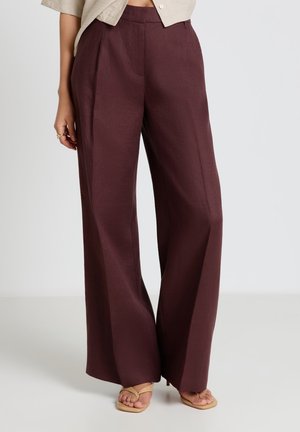 Donna che indossa pantaloni marroni a vita alta e gamba larga abbinati a sandali beige con tacco e punta aperta e top beige corto.