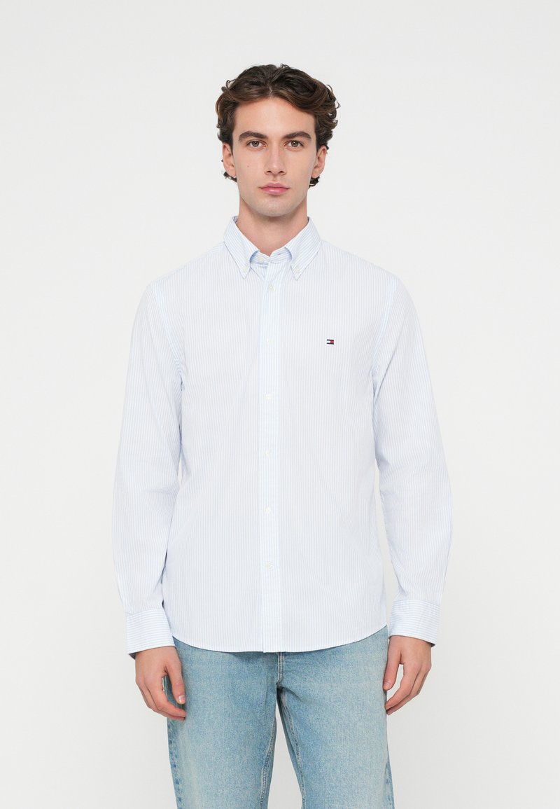 Ανοιχτό μπλε ριγέ πουκάμισο με γιακά, διαθέτοντας ένα μικρό λογότυπο στο στήθος. Κατασκευασμένο από ελαφρύ ύφασμα με μακριά μανίκια.