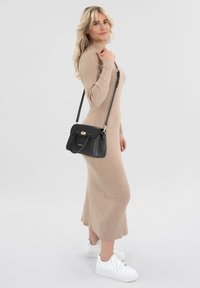 Abito lungo a maniche lunghe beige a coste con una silhouette aderente. Borsa a tracolla in pelle nera con accessori dorati. Sneaker bianche.