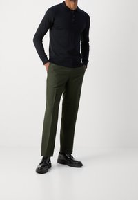 Polo a maniche lunghe nera con chiusura a bottoni, abbinata a pantaloni verdi oliva e scarpe nere stringate. Design semplice e forma aderente.