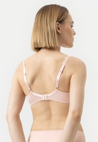 Vaaleanpunainen liivi, jossa on pitsisomisteita olkaimissa, säädettävät kiinnikkeet ja saumaton takasuunnittelu, valmistettu sileästä, kevyestä kankaasta.