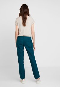 Tealfärgade linbyxor med rak passform, med bakfickor och en subtil textur. Matchas med en ljusbeige topp med kort ärm.