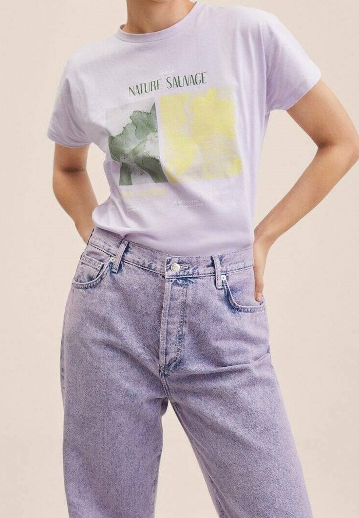 Personne portant un t-shirt violet clair avec des imprimés verts et jaunes et le texte "Nature Sauvage,", associé à un jean en denim violet taille haute.