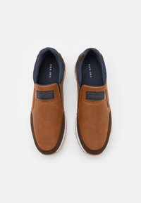 Braune Slipper aus strukturiertem Obermaterial, mit marineblauen Akzenten am Kragen und einer weißen Sohle. Verfügt über ein Logofähnchen an der Seite.