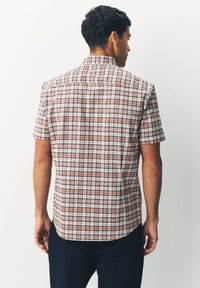 Chemise à manches courtes dans un motif à carreaux multicolores avec des nuances de rose, bleu et blanc, dotée d'un col boutonné et d'un ourlet droit.