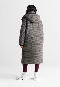 Garšs pūkains mētelis brūnas rūtiņas rakstā, ar kapuci, kvadrātveida siluetu un quilted tekstūru. Apvienots ar vīna krāsas legingiem un baltām sporta apaviem.