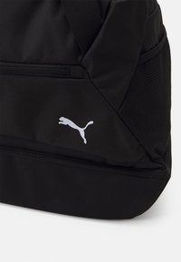 Sac à dos noir fabriqué en tissu durable, avec une poche zippée, des accents en maille et un logo Puma blanc. Design angulaire, texture légère.