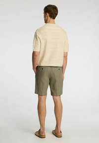 Krēmkrāsas īssa roka adīta džemperis ar teksturētām svītrām, kombinēts ar olīvzaļām šortiem ar aizmugures kabatām un brīvu piegriezumu.
