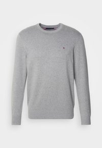 Grijze gebreide trui met een ronde hals, geribbelde manchetten en zoom. Heeft een klein logo in rood, wit en blauw op de borst. Zachte textuur.