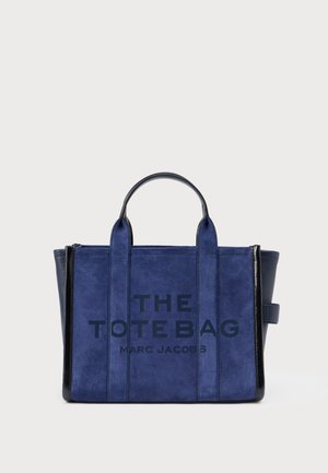 Marineblauwe suède totebag met zwarte lederen accenten, met de tekst "THE TOTE BAG" en "MARC JACOBS" duidelijk zichtbaar aan de voorkant.