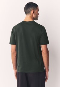 Tume roheline puuvillane T-särk ümmarguse kaelusega ja lühikeste varrukatega, sileda tekstuuri ja tavapärase istuvusega, vaadeldav tagantpoolt.