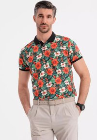Kortærmet polo skjorte lavet af stof med et levende blomsterdesign med røde og hvide blomster på en grøn baggrund, sort krave.