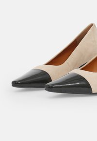 Beige velúr, hegyes orrú magassarkúk fekete lakk bőr orral. Simaság, elegáns dizájn alacsony kivágású pánttal.