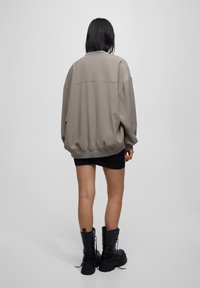 Chaqueta taupe de gran tamaño con escote redondo, hombros caídos y puños de canalé, combinada con una minifalda negra y botas negras hasta la rodilla.