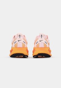 Las zapatillas de running de Nike presentan una parte superior rosa con acentos naranjas, paneles de malla texturizada y una suela de goma para un mejor agarre, vistas desde la parte trasera.