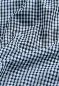 Țesătură din bumbac cu un model de gingham alb și albastru, cu carouri mici, textură moale și un aspect ușor șifonat.
