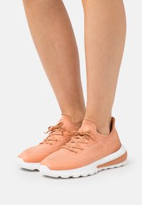 Scarpe da ginnastica color pesca con parte superiore in knit texturizzato, chiusura con lacci e suola bianca caratterizzata da un accentopuntato per grip e supporto.
